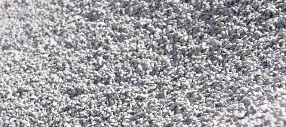 A close-up view of 5-7mm drainage aggregate, a versatile material used for effective water management. The aggregate consists of small, rounded stones in various shades of gray and brown, providing a textured and natural appearance. This size is ideal for applications such as drainage systems, garden landscaping, and construction projects. The aggregate is shown spread out evenly, demonstrating its ability to facilitate water flow while preventing soil erosion. Its compact composition ensures durability and long-lasting performance.