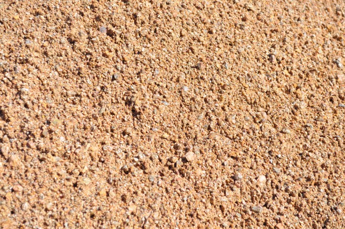 A close-up view of pink decomposed granite, a crushed stone material commonly used for landscaping purposes. The granite particles are varying shades of pink, ranging from pale to deep hues, giving the surface a textured and visually appealing appearance. The smooth and finely crushed texture of the granite creates a stable and compacted surface ideal for pathways, driveways, and garden beds. Available at Parklea Sand & Soil Australia.