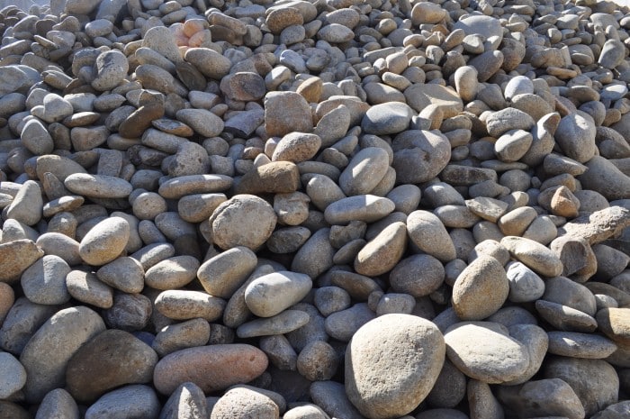 A close-up view of large river pebbles in shades of gray, beige, and brown. These smooth stones measure approximately 150-300mm in size and are commonly used for landscaping and decorative purposes. Their natural colors and texture add a touch of elegance to outdoor spaces such as gardens, pathways, and water features.