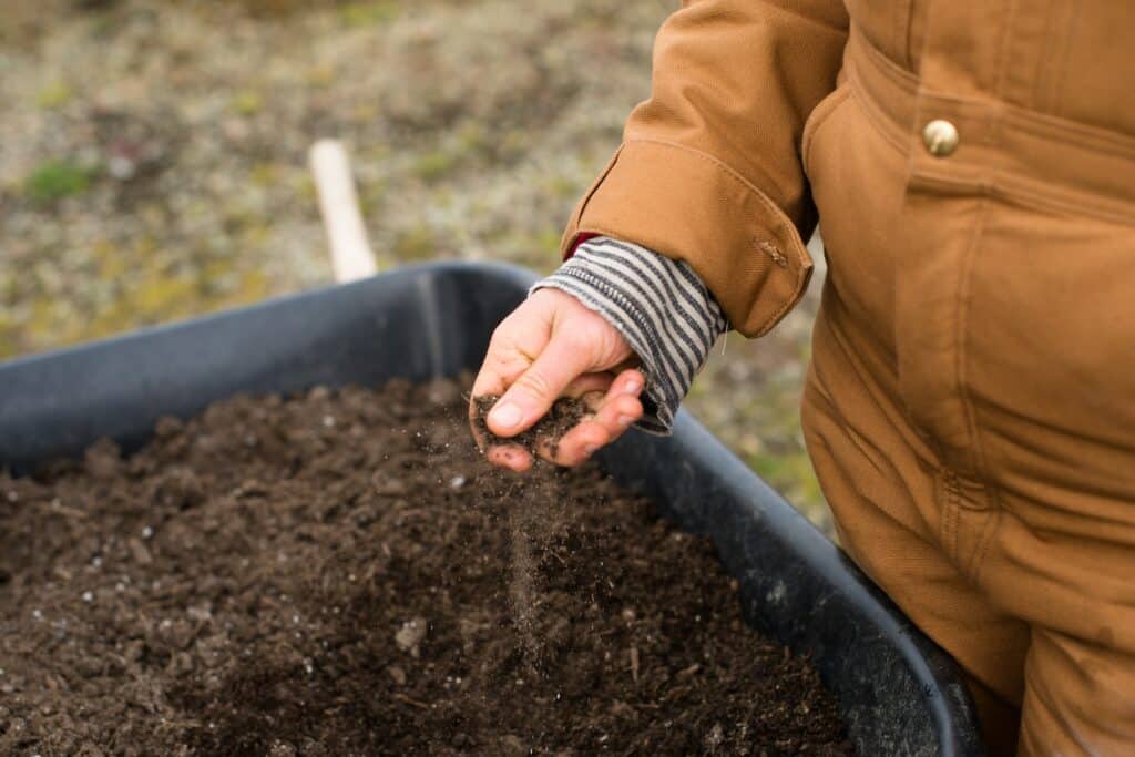 Person in brown jacket holding a handful of soil, checking quality of soil. Quality soil from Parklea Sand & Soil Australia. 